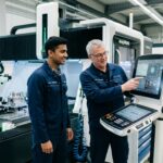 Indian apprentice and German technician in modern manufacturing plant during mechatronics training